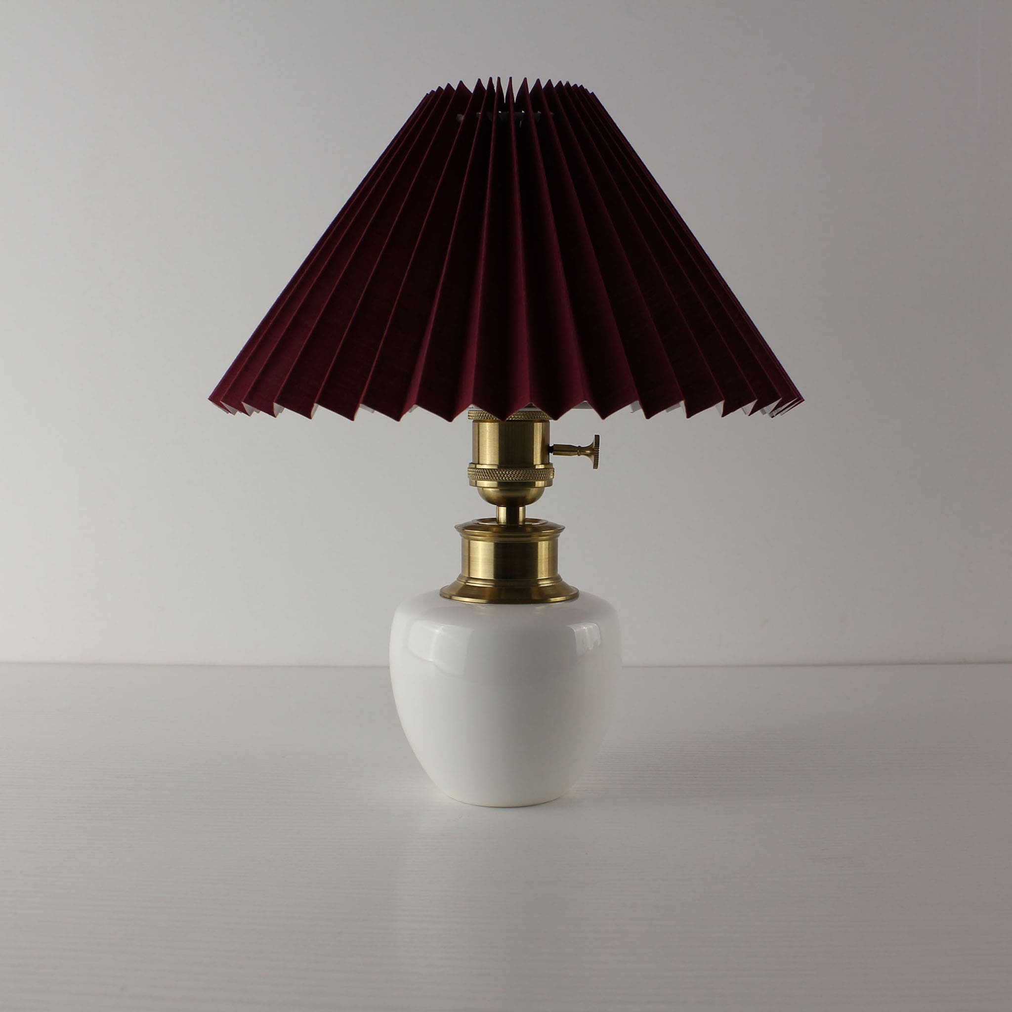 Mid-century modern cordless porcelain lamp with a burgundy red pleated shade, off.