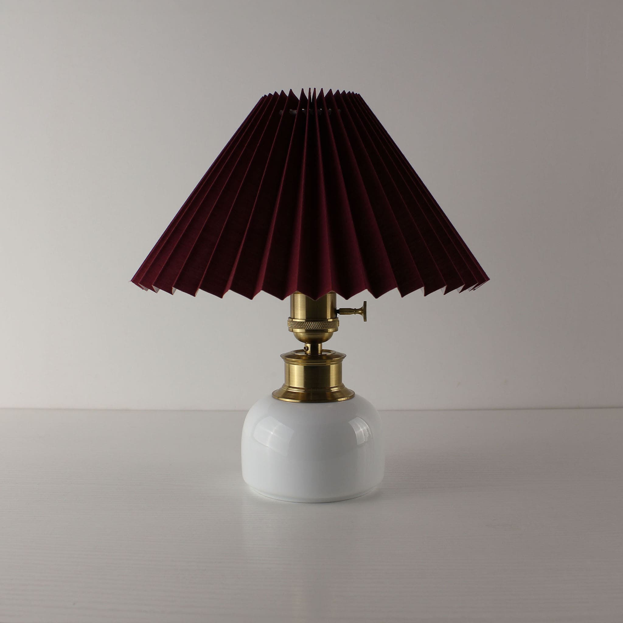 Vintage style battery operated lamp with wine red pleated shade and brass accents on a ceramic base.