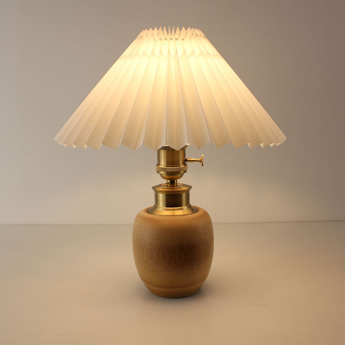 Warm glow white pleated shade bamboo lamp turned on, creating a cozy atmosphere for bedroom or hallway lighting.