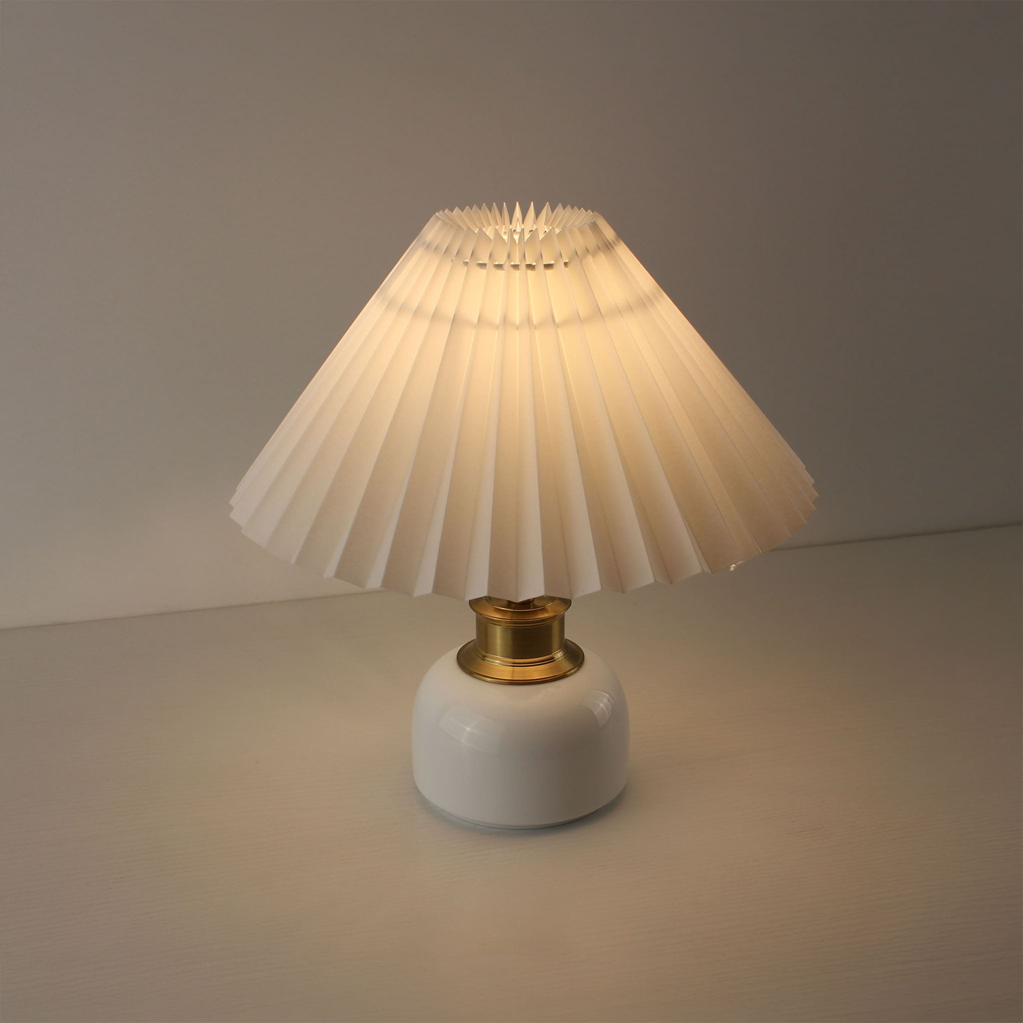 Elegant white pleated shade lamp with a warm glow, featuring a luxury ceramic base for bistro or bedroom lighting.