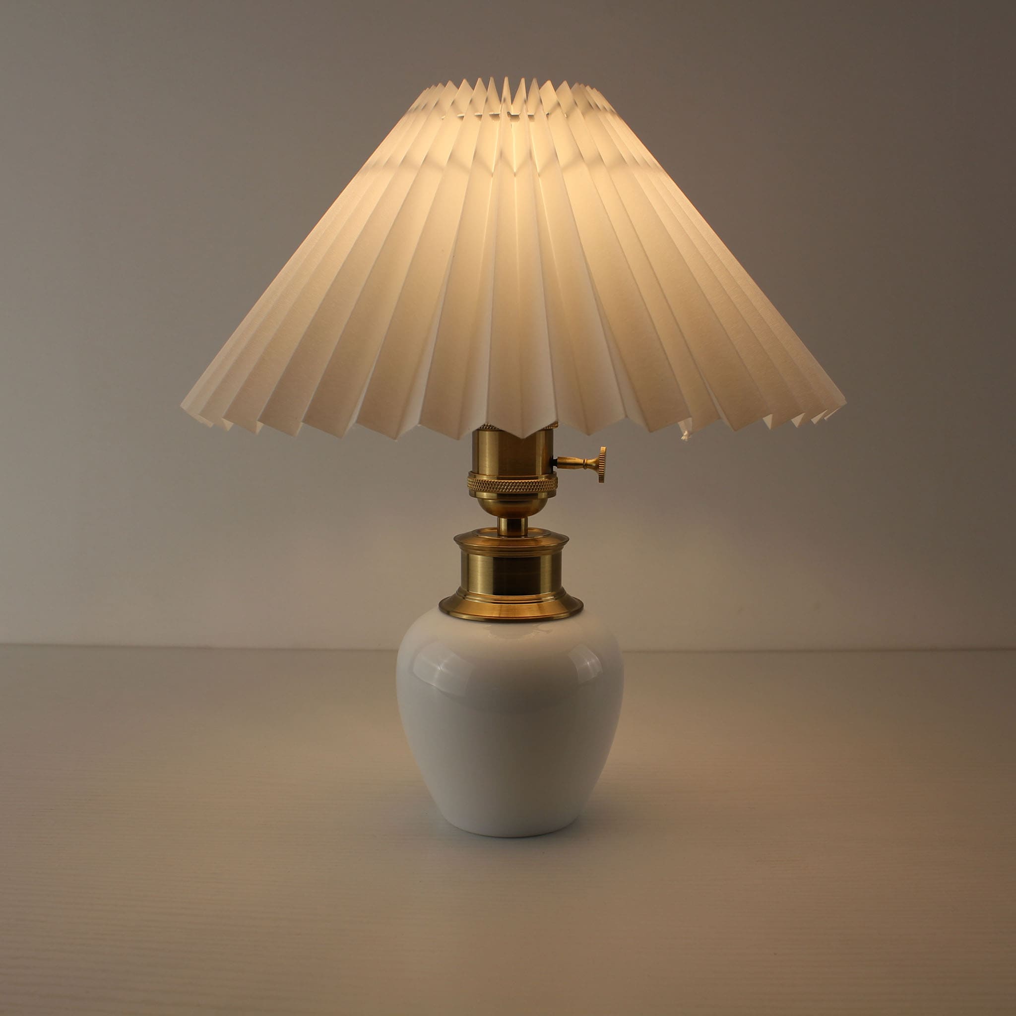 Portable cordless porcelain lamp with white pleated shade turned on, ideal for a cozy living room or cafe.