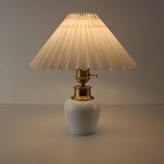 Portable cordless porcelain lamp with white pleated shade turned on, ideal for a cozy living room or cafe.