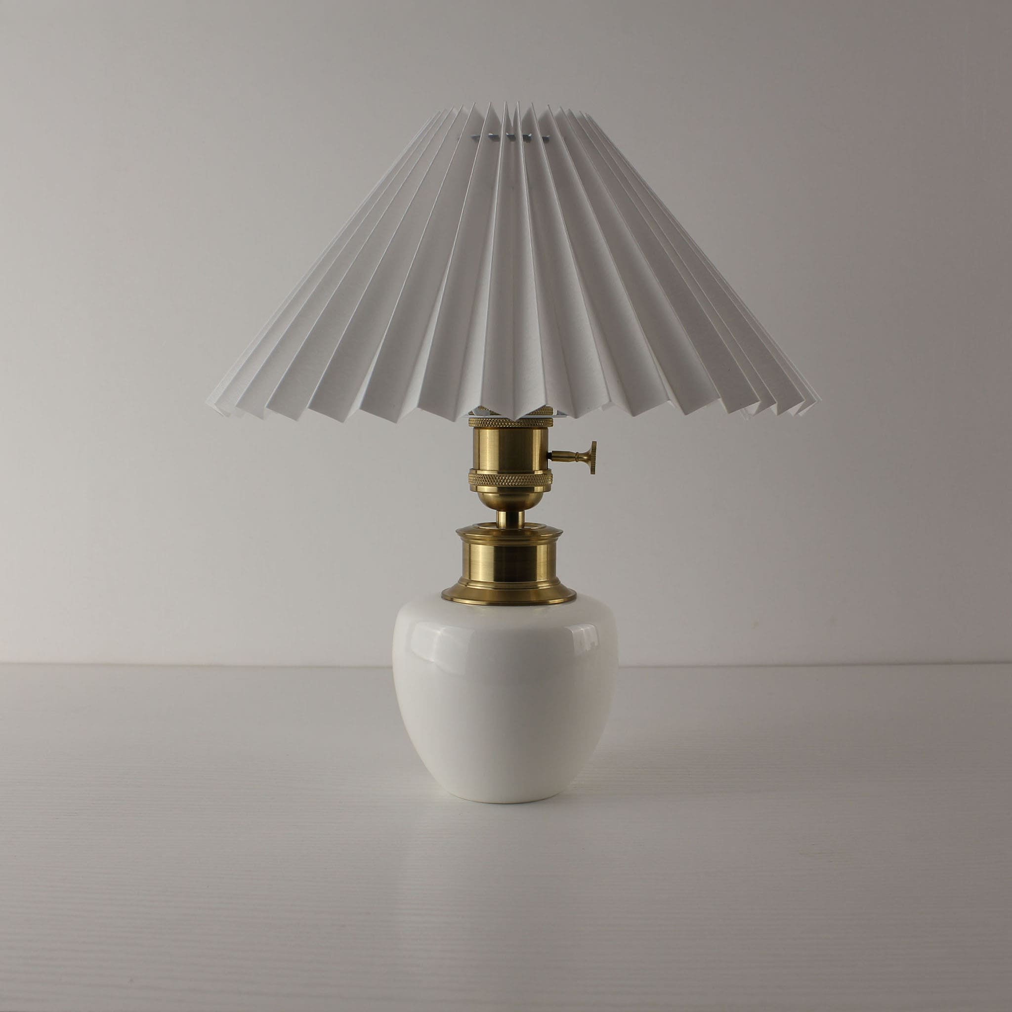 Handcrafted white porcelain cordless table lamp with a white pleated shade, turned off.