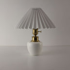 Handcrafted white porcelain cordless table lamp with a white pleated shade, turned off.