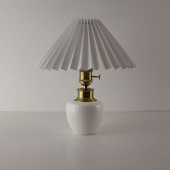Handcrafted white porcelain cordless table lamp with a white pleated shade, turned off.